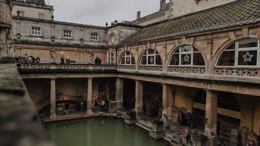 Băile Romane din Bath Anglia cu apa verde si arhitectura georgiană în fundal la apus